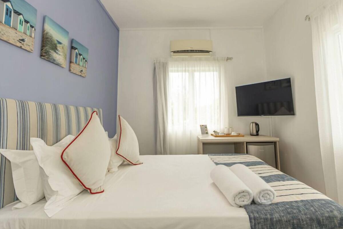 A hotel room with a bed, a desk, a television, and artwork on the wall.