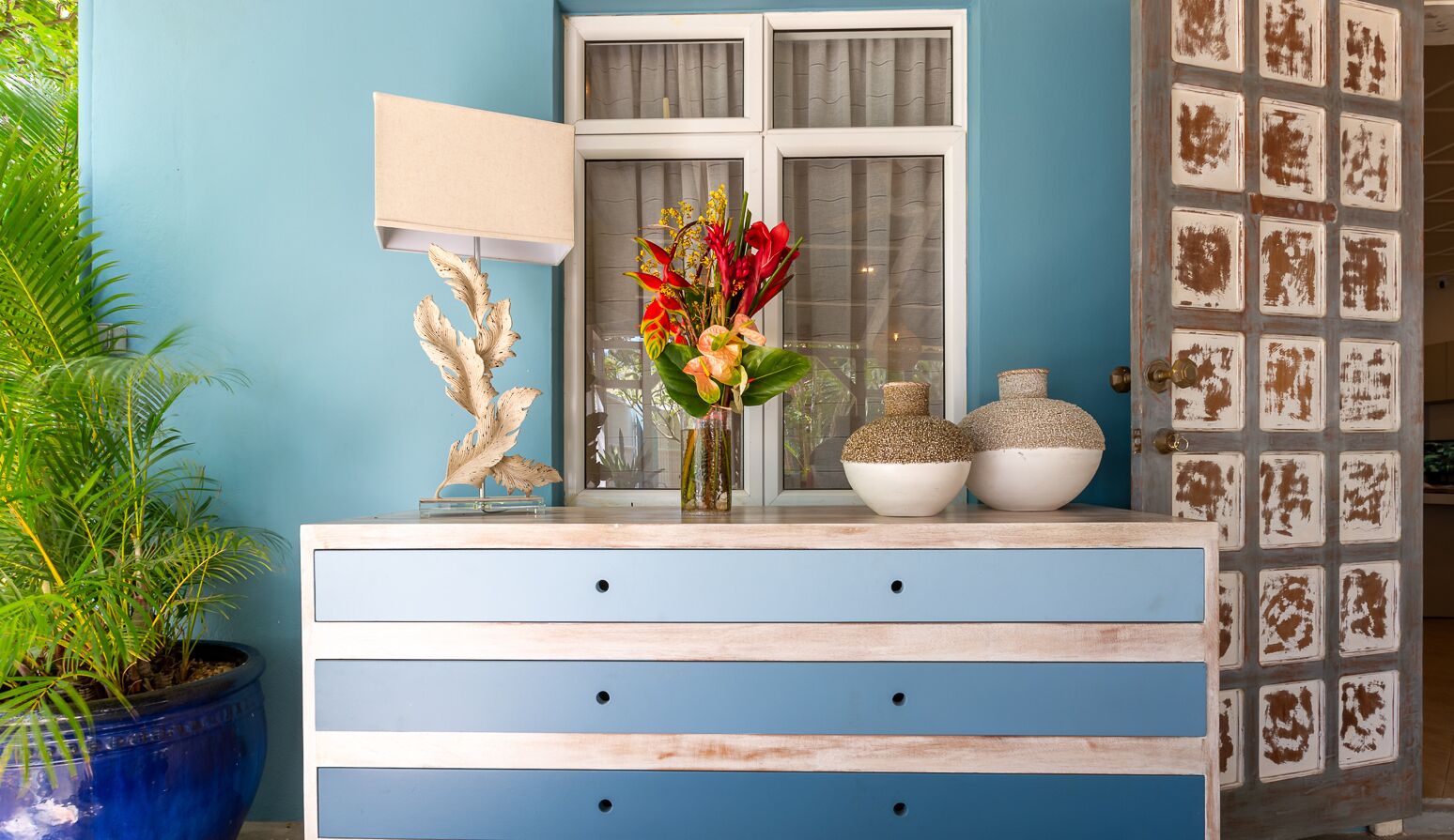 A blue dresser with three drawers, a vase with flowers, and decorative items on top.