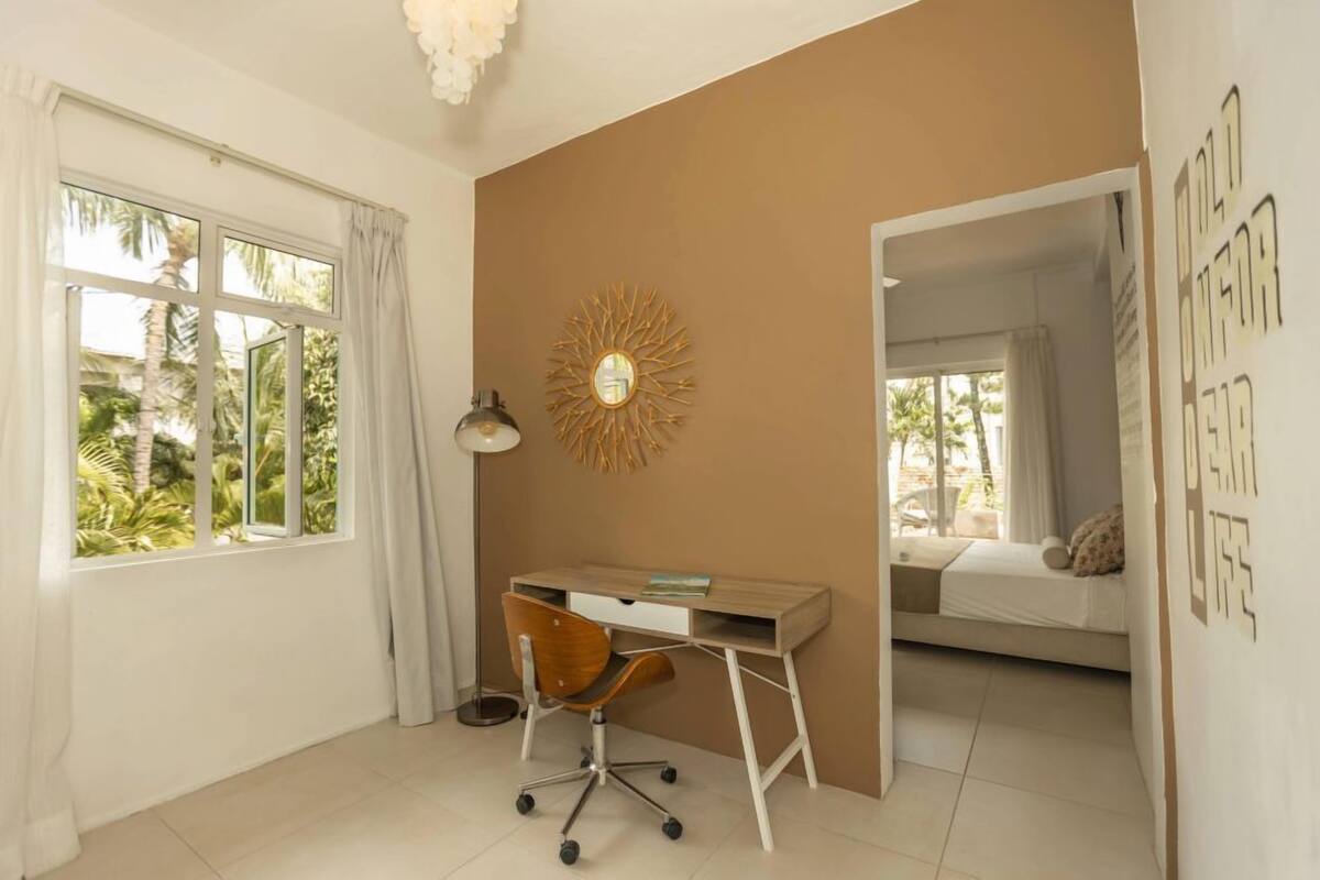 A bedroom with a bed, a desk with a chair, a window, and a wall with a sunburst decoration.