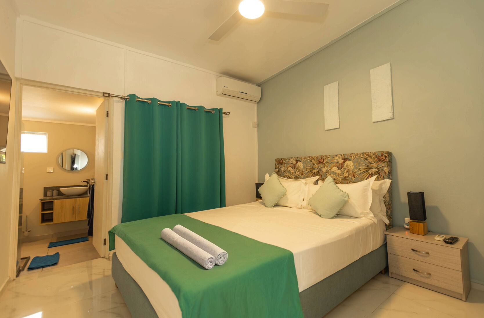 A neatly arranged bedroom with a bed, bedside table, and a bathroom visible through an open door.