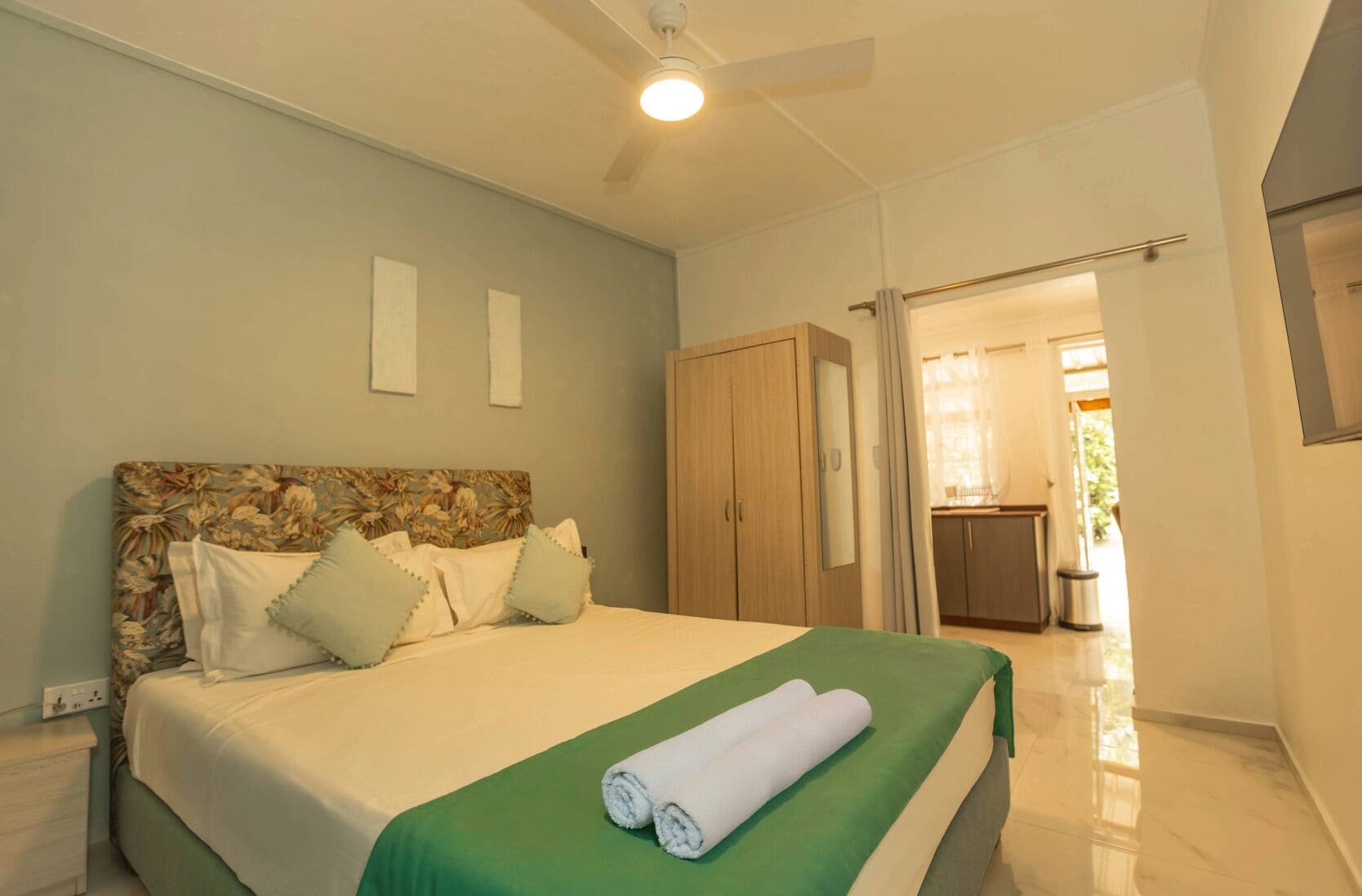 A bedroom with a bed, a green bedspread, and a ceiling fan.