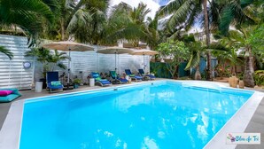A swimming pool with lounge chairs and umbrellas, surrounded by palm trees and a white fence. - Bleu de Toi - Boutique Guest House (Grand-Baie)