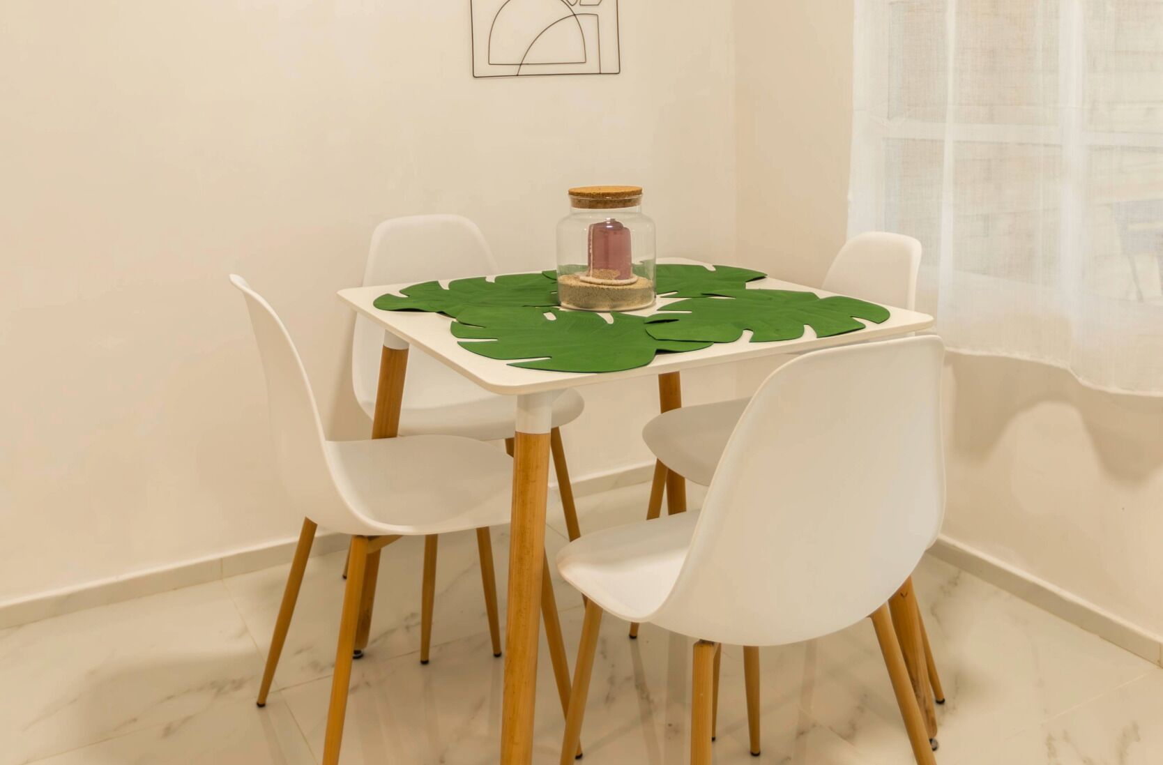 Un tavolo da pranzo con una tovaglia verde a motivi floreali, circondato da sedie bianche a gambe in legno.