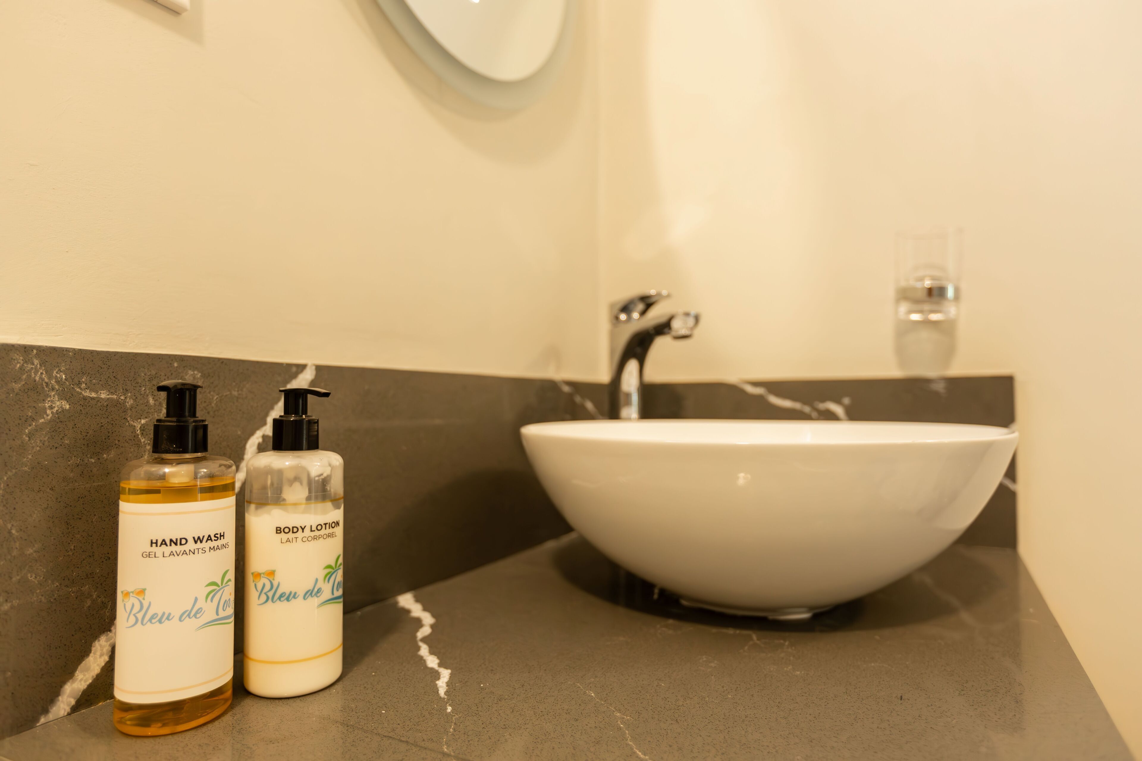 Un baño con un lavabo blanco, dos botellas de jabón de manos y crema corporal, y un espejo sobre el lavabo.