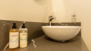 Un baño con un lavabo blanco, dos botellas de jabón de manos y crema corporal, y un espejo sobre el lavabo.