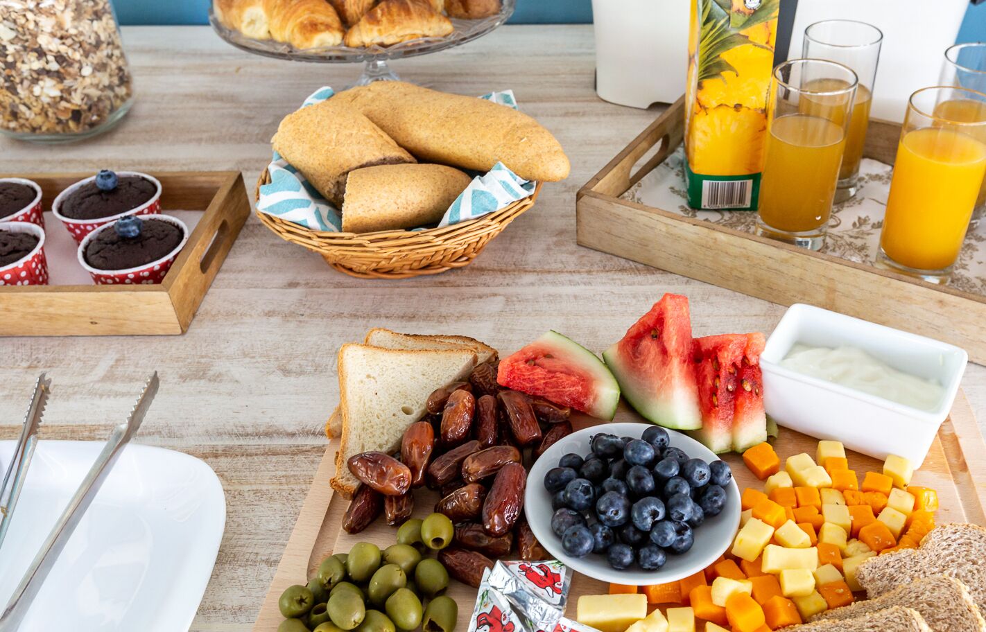 A breakfast buffet with bread, pastries, fruits, and beverages.