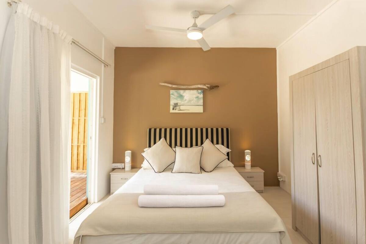 A bedroom with a bed, bedside tables, a ceiling fan, a nightstand, a wardrobe, and a painting on the wall.