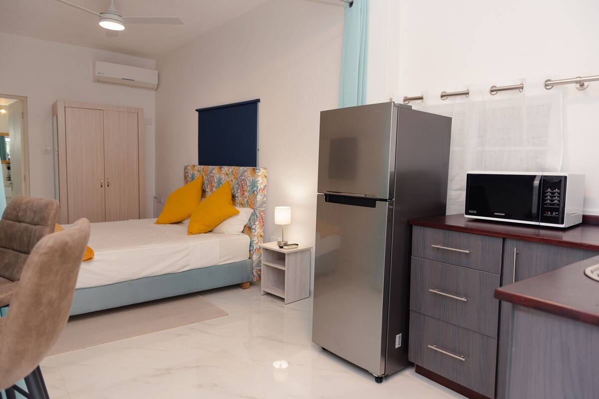 A bedroom with a bed, a nightstand, a refrigerator, a microwave, and a wardrobe.