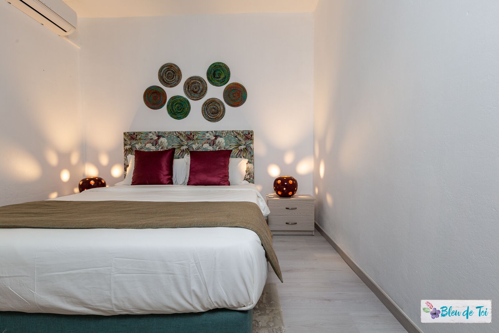 Una camera da letto con un letto, cuscini, un comodino e decorazioni a parete.