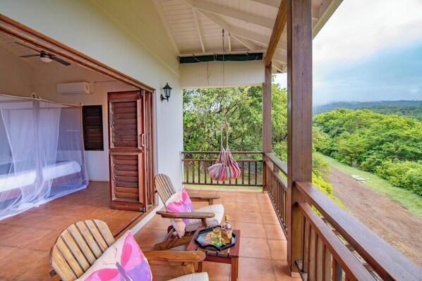A balcony with a wooden railing, a hanging chair, and a table with a tray. - Cabier Ocean Lodge (St. Andrew)