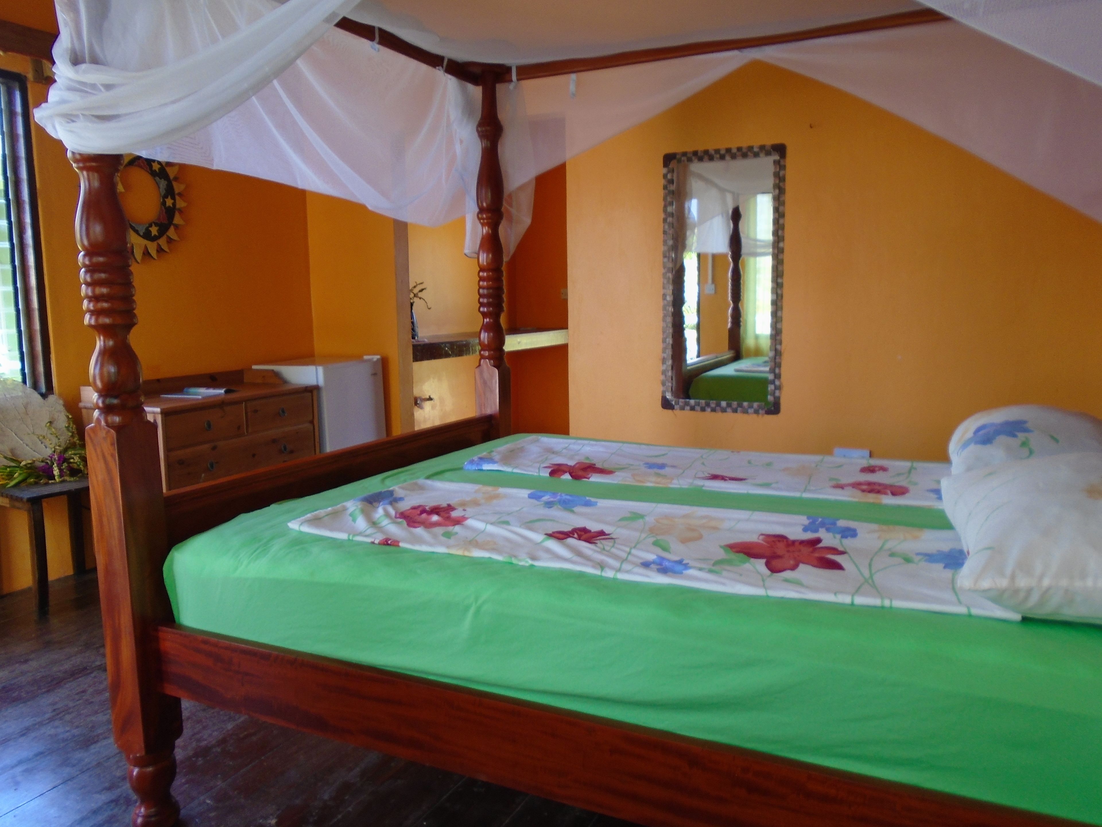 Une chambre à coucher avec un lit à baldaquin, une couvre-lit verte, une commode en bois et un miroir au mur.