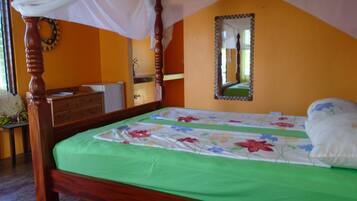 Une chambre à coucher avec un lit à baldaquin, une couvre-lit verte, une commode en bois et un miroir au mur.