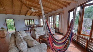 A spacious living area with a hammock, large windows, and a wooden ceiling.