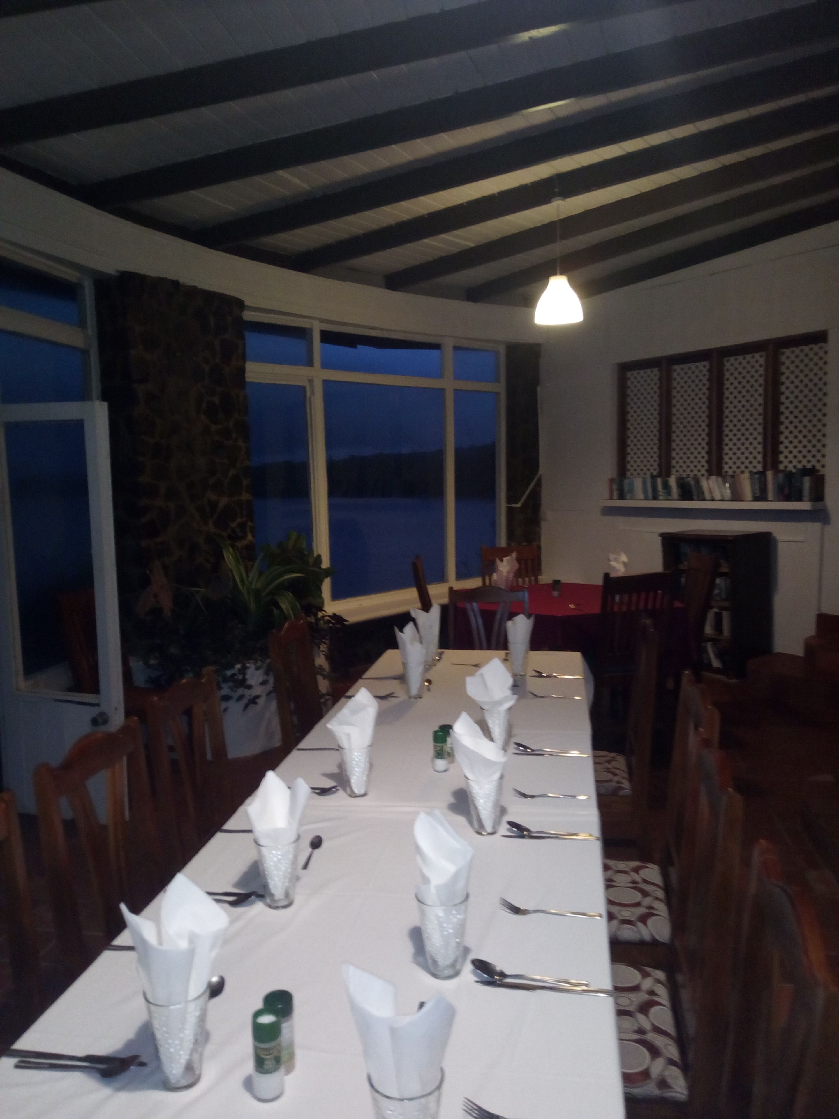Un espace repas avec une longue table dressée pour le repas, de grandes fenêtres et un pilier en pierre.