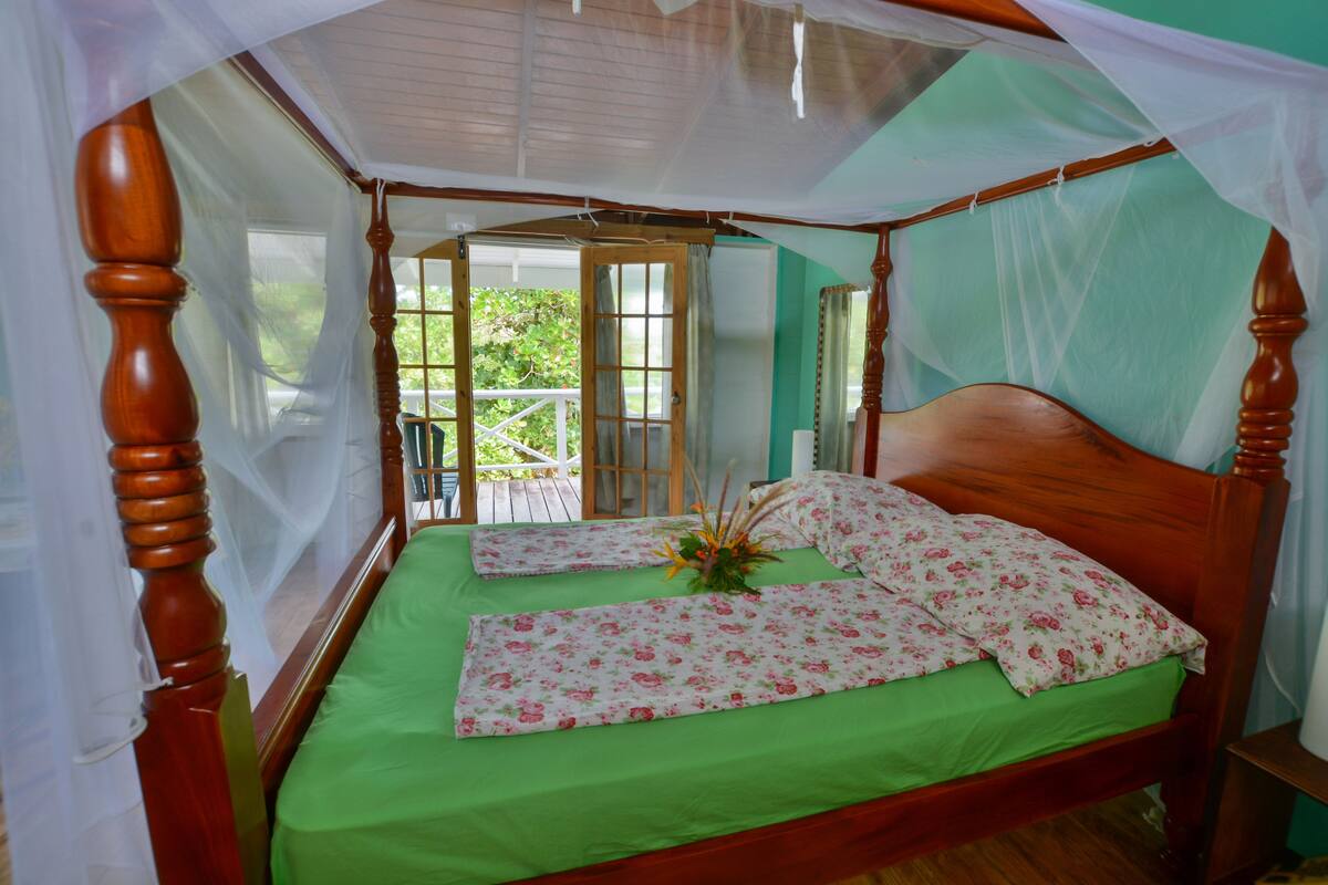 Uma cama de dossel com colcha verde e almofadas florais, uma cabeceira de madeira e um baldaquim.