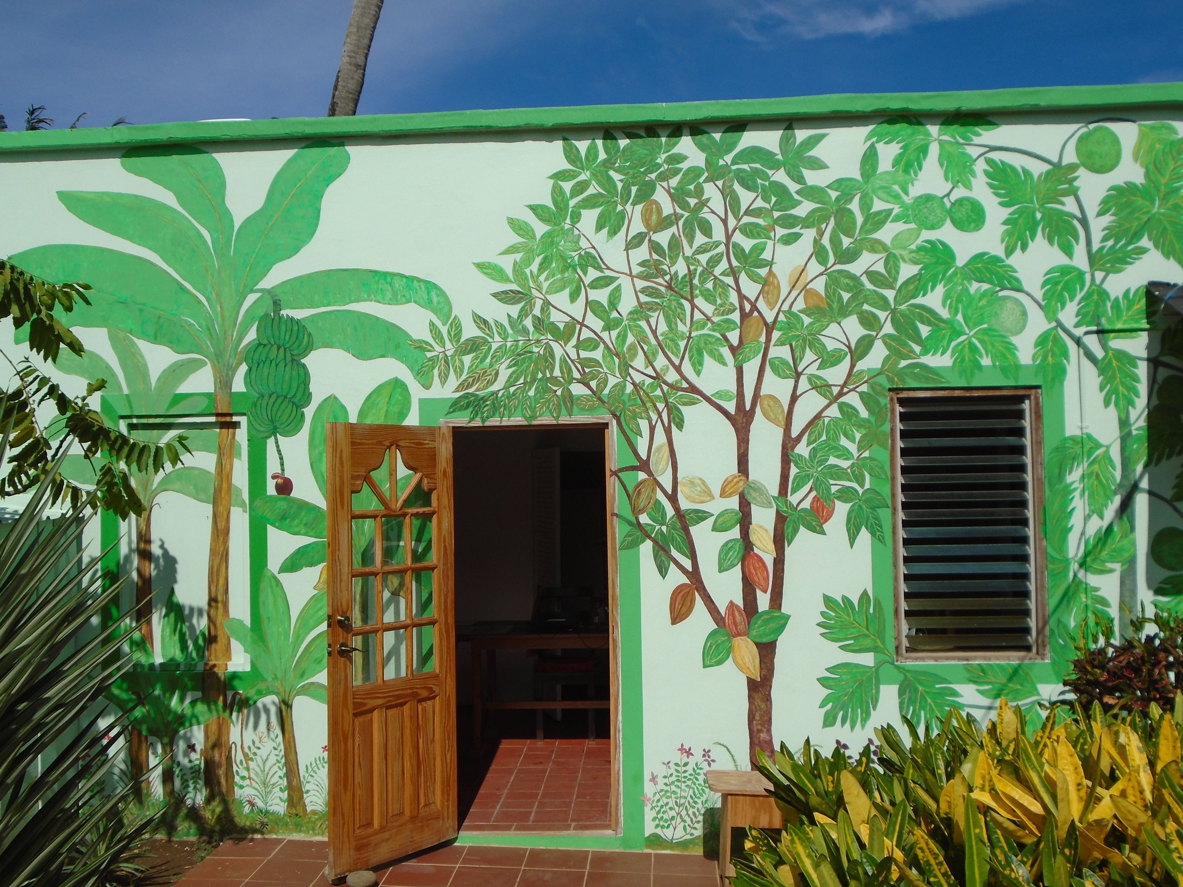 Un edificio con un murale di piante tropicali e una porta in legno.
