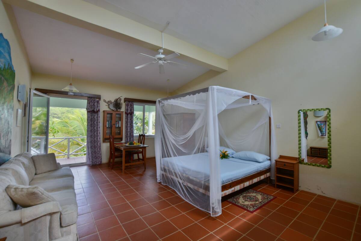 Quarto com cama de dossel, sofá, mesa de jantar e ventilador de teto.