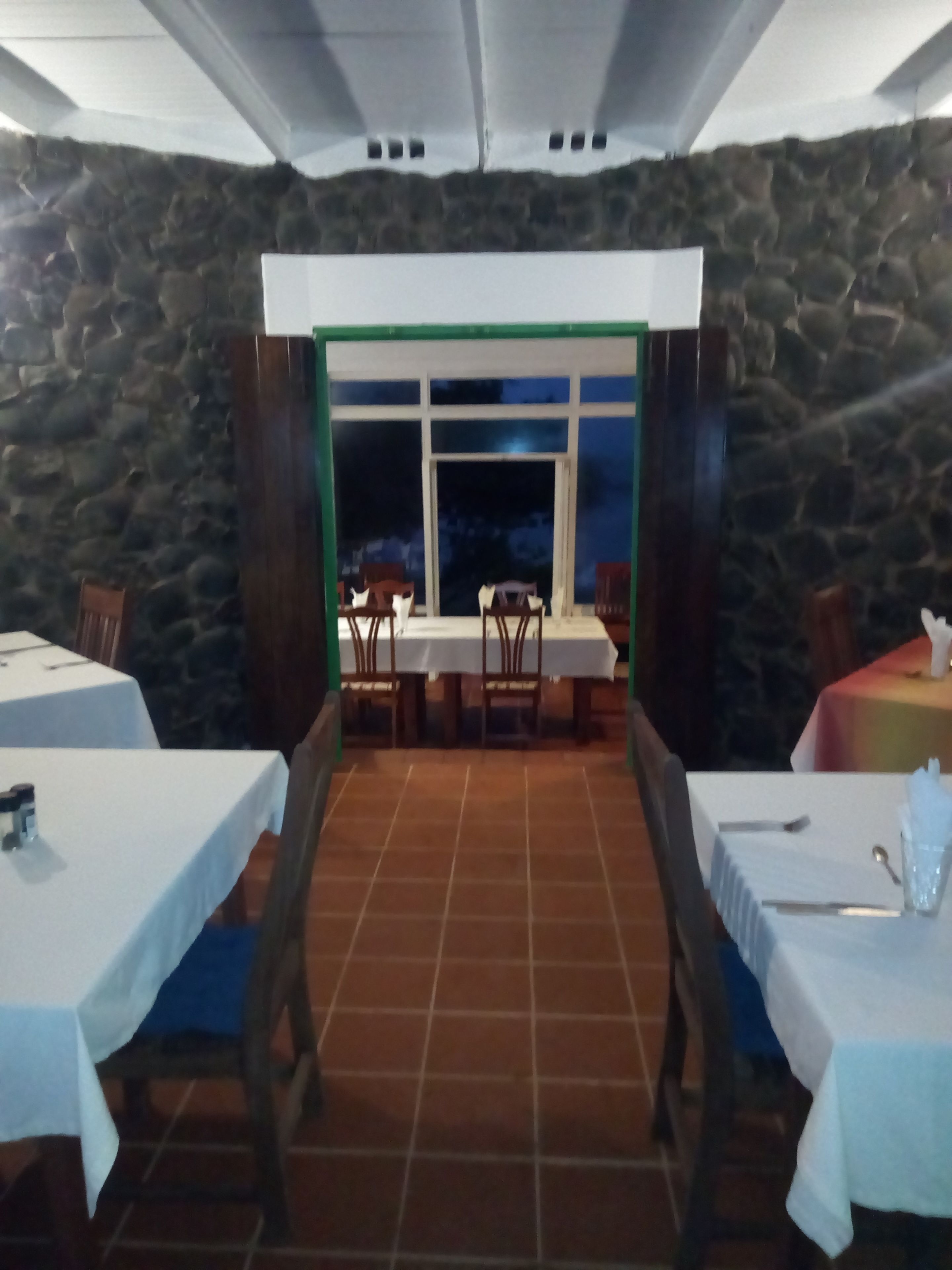 A restaurant with stone walls, a tiled floor, and tables set for dining.