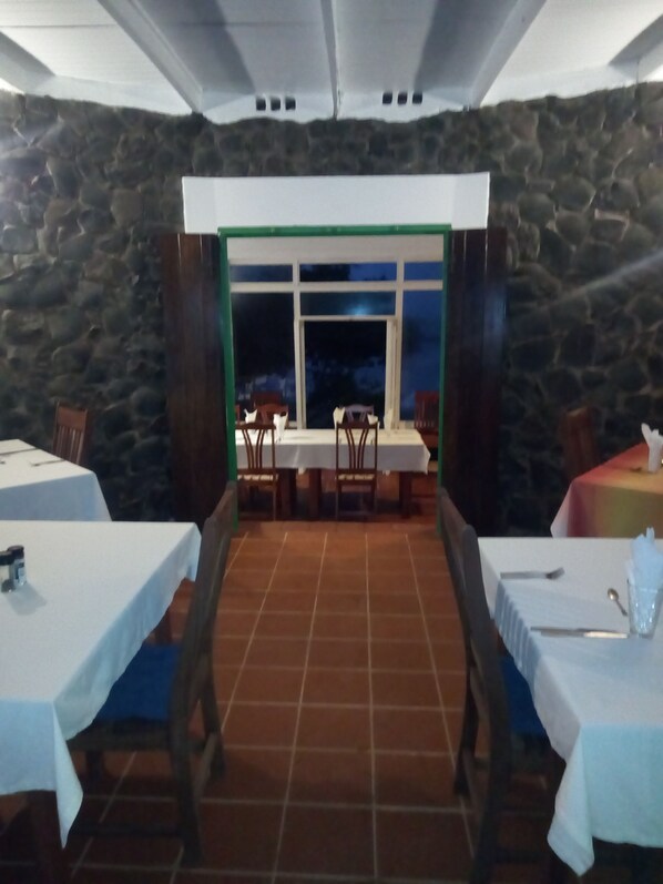 A restaurant with stone walls, a tiled floor, and tables set for dining. - Cabier Ocean Lodge (St. Andrew)