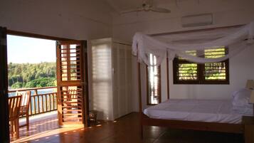 Un dormitorio con cama, ventilador de techo, ventana con cortinas y vistas al exterior.