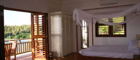 Une chambre à coucher avec un lit, un ventilateur de plafond, une fenêtre avec des rideaux et une vue sur l’extérieur.