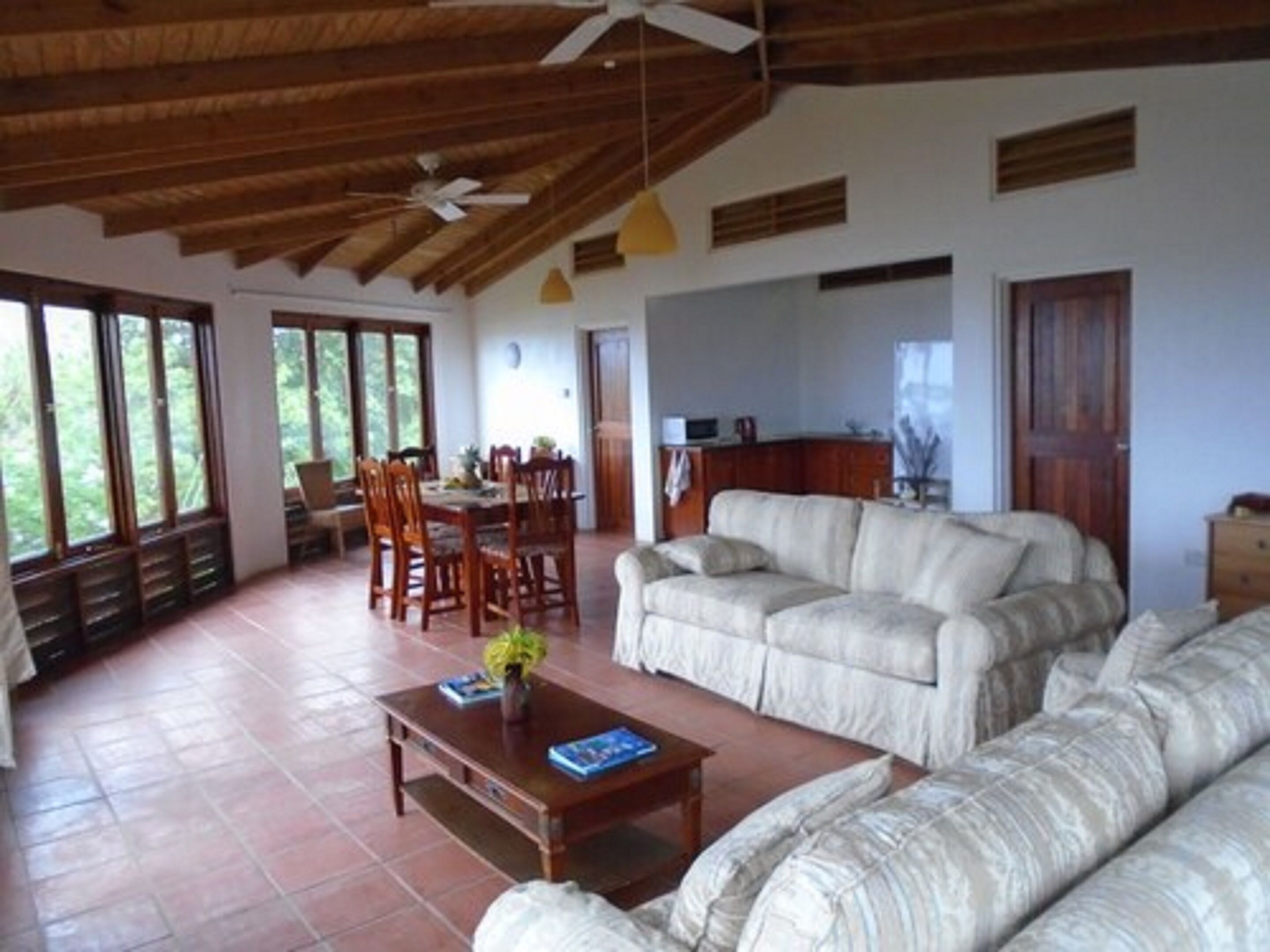 Amplia sala de estar con un conjunto de sofás, una mesa de comedor con sillas y una zona de cocina con microondas.