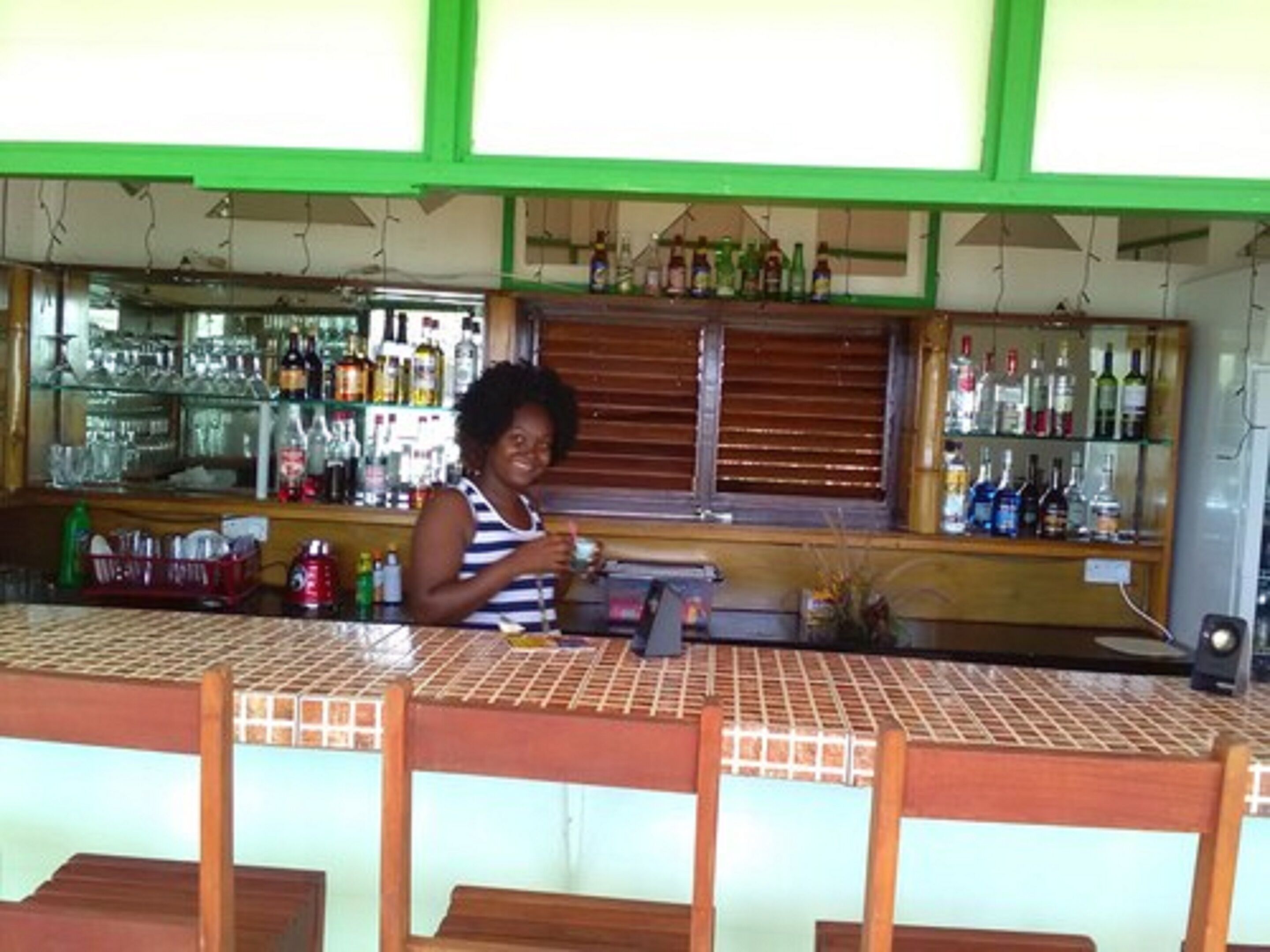 Zona de bar con mostrador, estantes con botellas y una ventana con persianas.