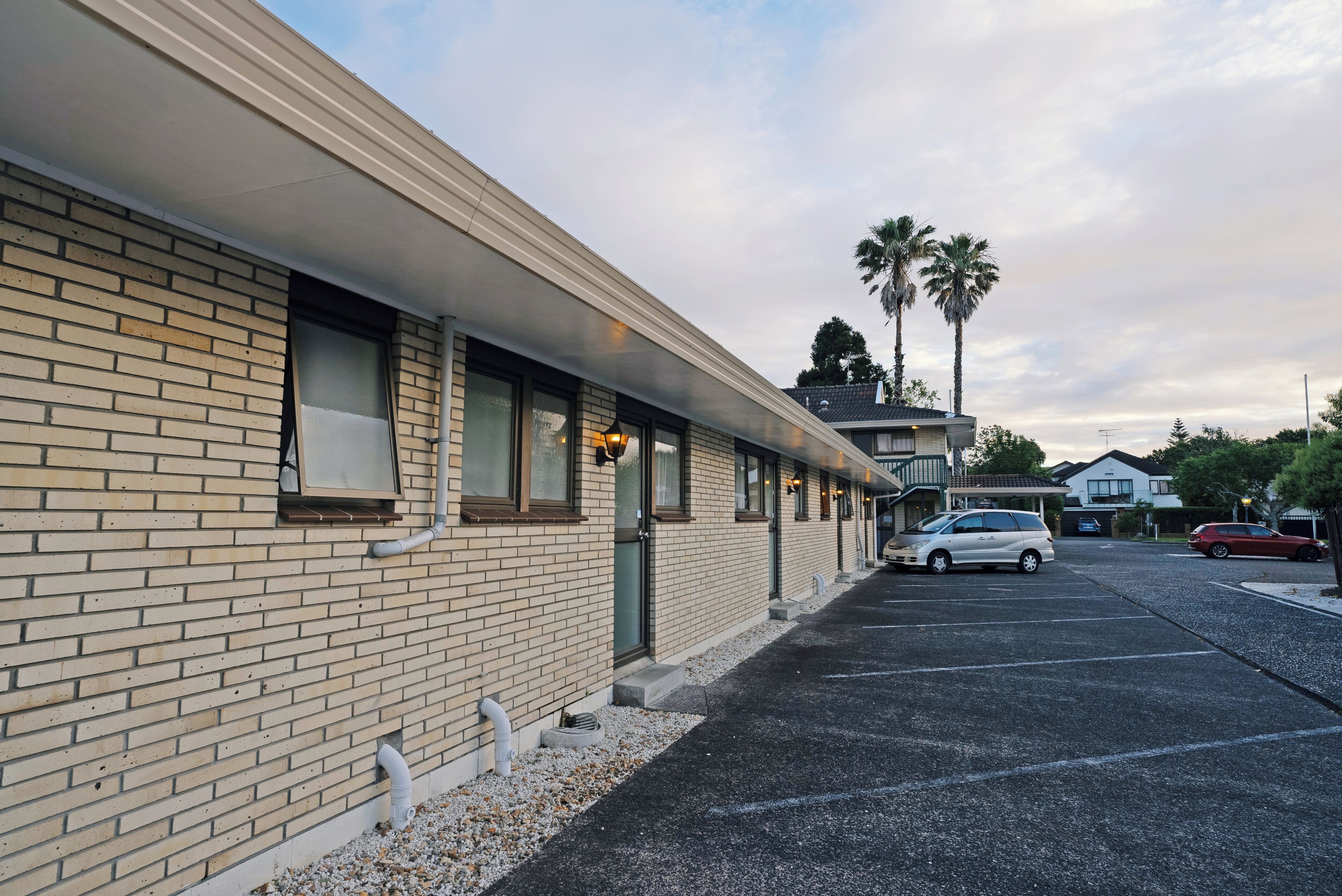 Un motel avec une façade en briques, un parking et des palmiers en arrière-plan.