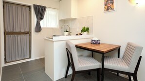 Une cuisine compacte avec un coin repas, une fenêtre avec des rideaux, un luminaire fixé au mur et un tableau encadré.