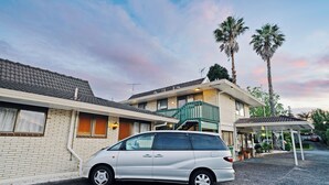 Un bâtiment à deux étages doté d’un espace extérieur couvert, d’une voiture garée et de palmiers.