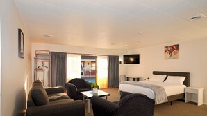 Une chambre d’hôtel avec un lit, deux fauteuils, une petite table, un téléviseur et un tableau au mur.