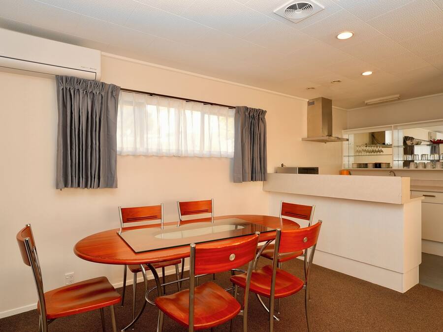A dining area with a round table and six chairs, a kitchen with a white countertop, and a window with curtains.