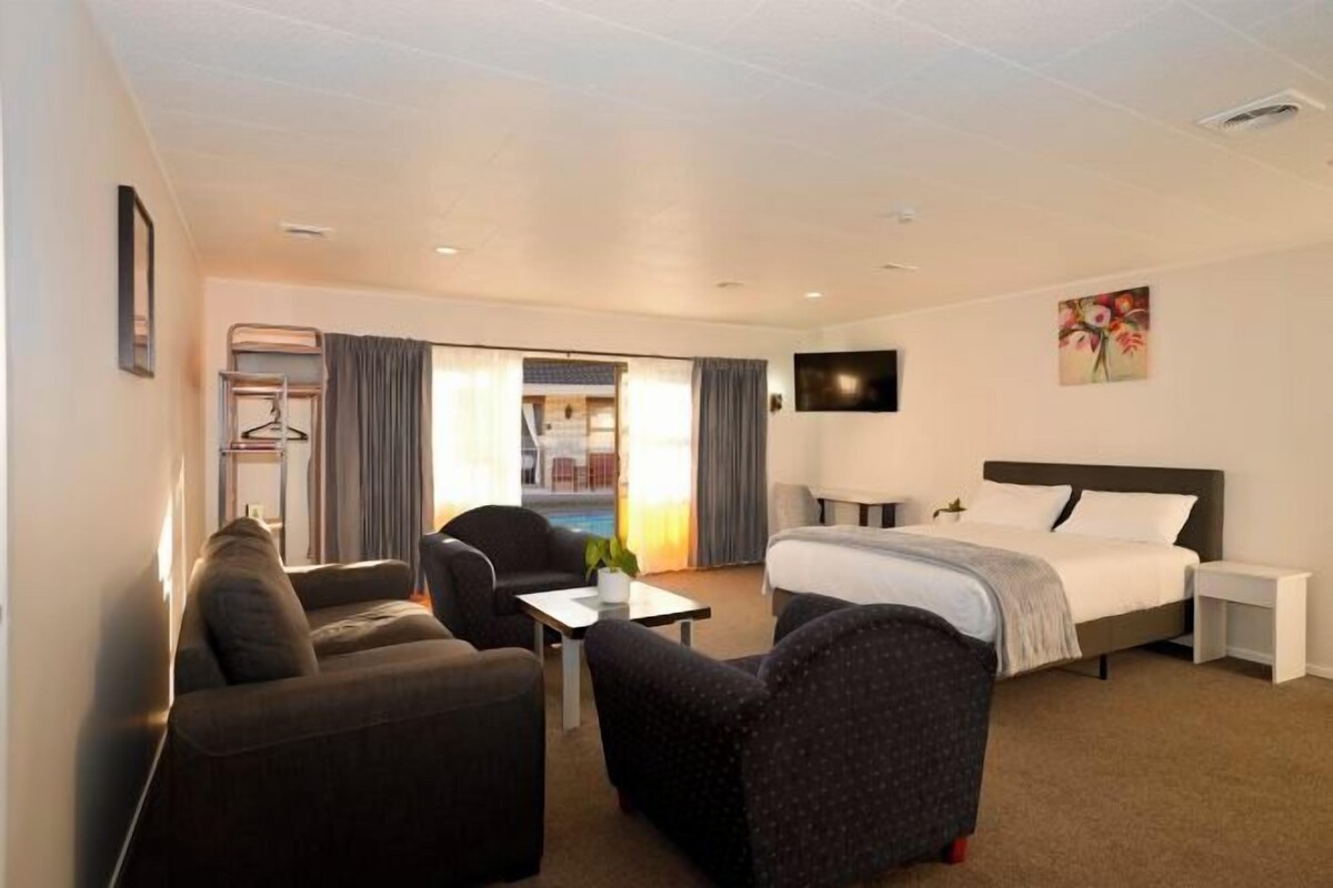 Habitación de hotel con cama, dos sillones, escritorio y televisor.