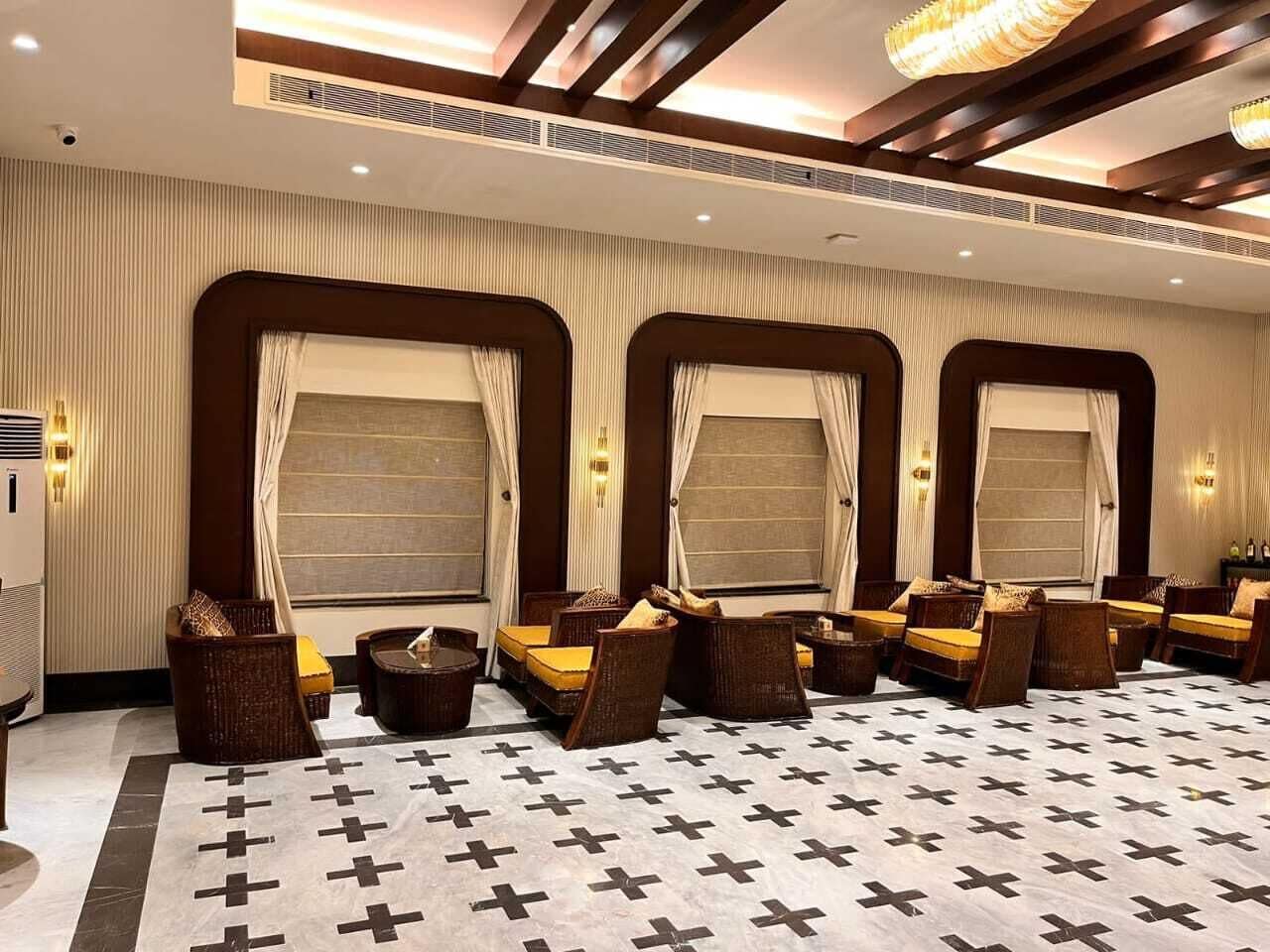 Habitación de hotel con un amplio espacio de estar, varias ventanas con cortinas y un suelo estampado.