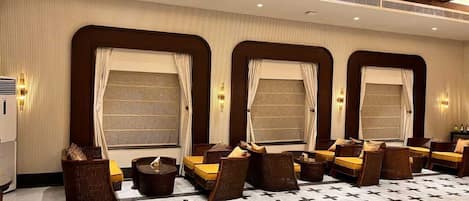 A hotel room with a large seating area, multiple windows with curtains, and a patterned floor.