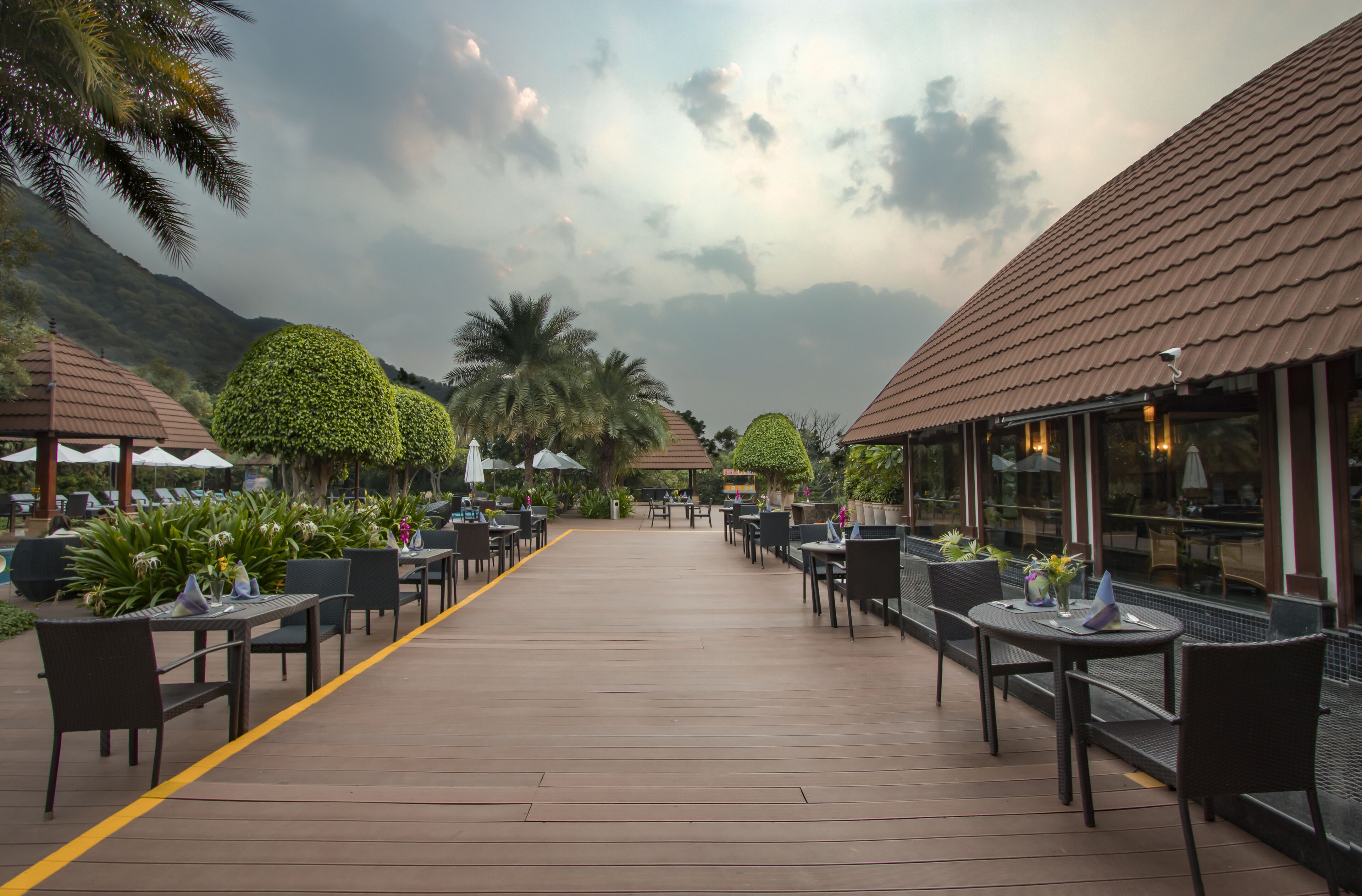 An outdoor dining area with tables and chairs, surrounded by greenery and a mountain backdrop.