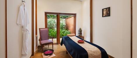 Une pièce comprenant une table de massage, une chaise, un porte-serviettes et une statue.
