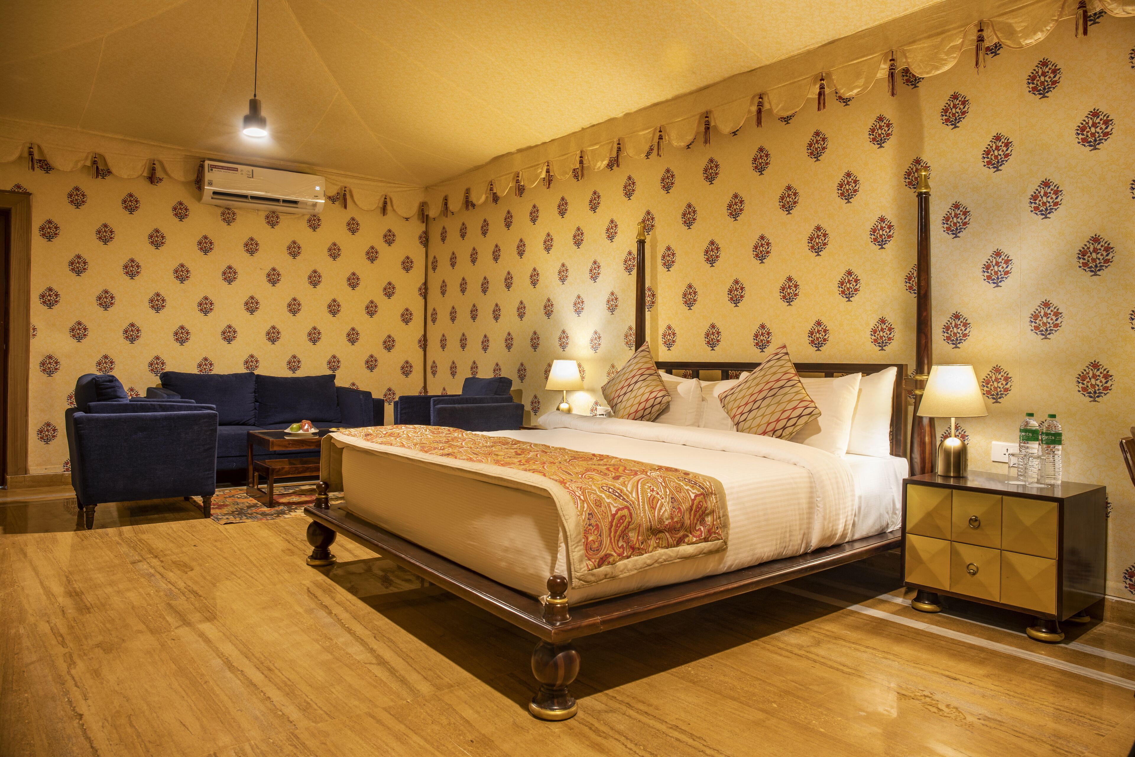Una habitación de hotel con una cama grande, un sofá, una mesita de noche y una lámpara.
