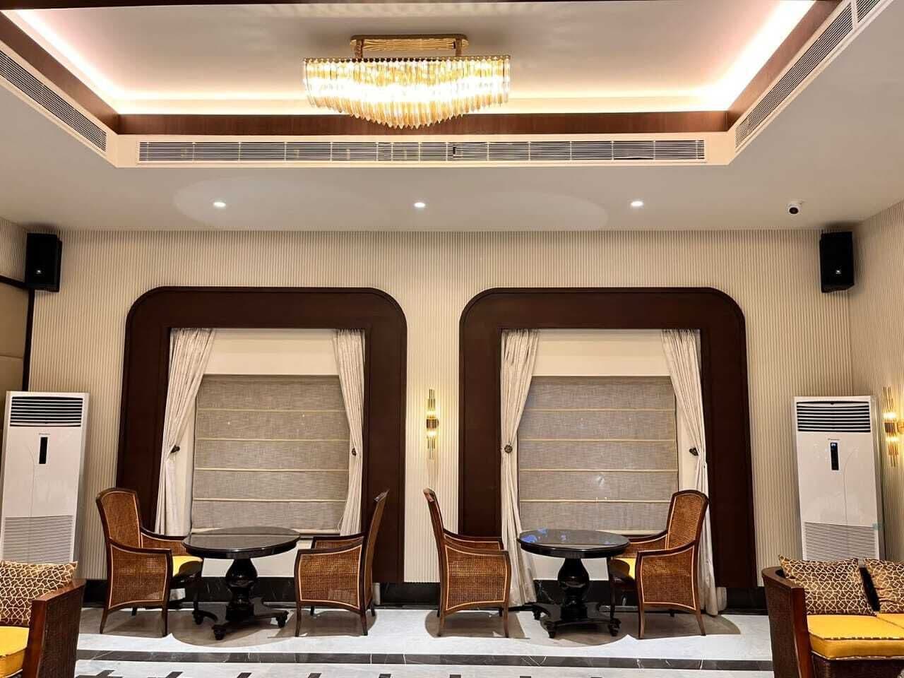 Een hotelkamer met twee eettafels, elk omringd door vier stoelen. Aan weerszijden van de kamer bevinden zich airconditioningsunits.