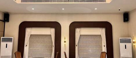 Habitación de hotel con dos mesas de comedor, cada una rodeada por cuatro sillas. Hay unidades de aire acondicionado a ambos lados de la habitación.
