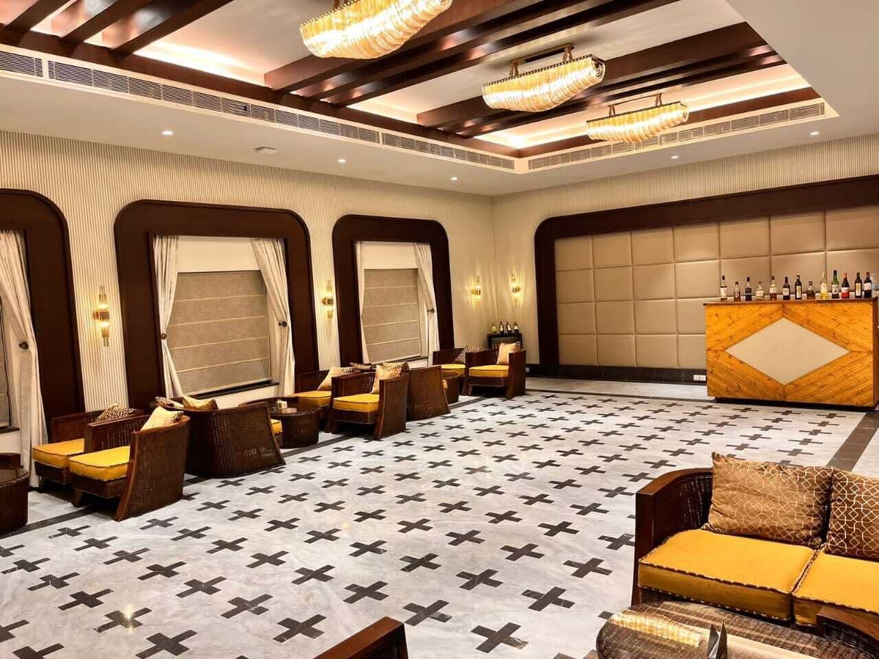 Eine Hotelhalle mit einem gemusterten Boden, einer Sitzecke mit Sofas und Sesseln, einer Bar mit Flaschen und einer großen Wand mit geometrischem Design.