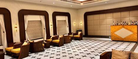 Eine Hotelhalle mit einem gemusterten Boden, einer Sitzecke mit Sofas und Sesseln, einer Bar mit Flaschen und einer großen Wand mit geometrischem Design.