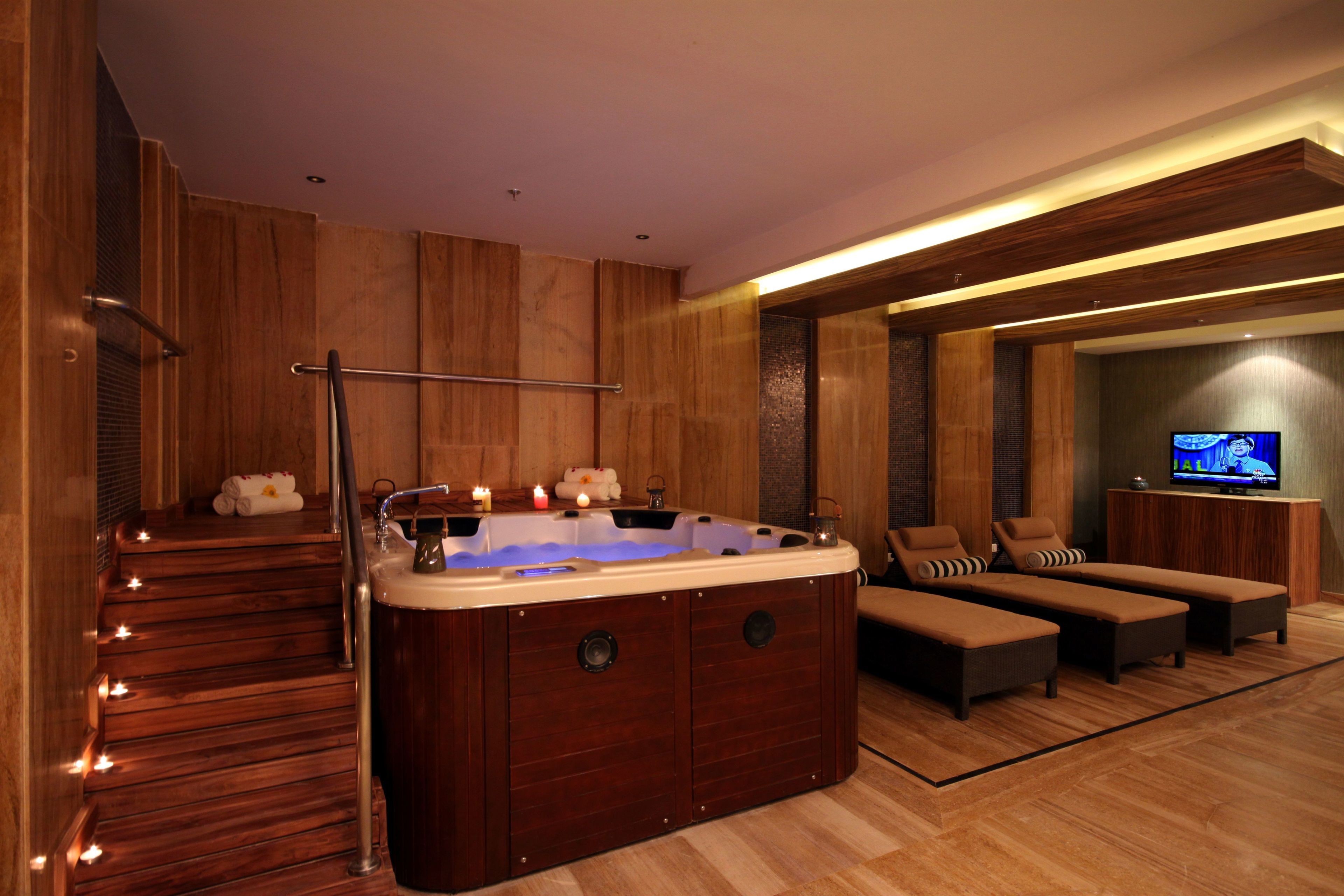 A modern spa area with a hot tub, wooden flooring, and a television.