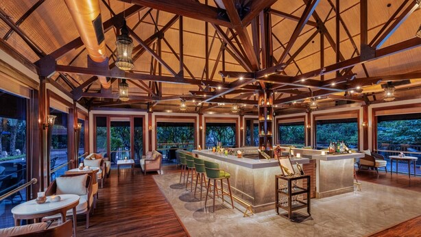 A spacious bar area with high ceilings and large windows overlooking a lush garden. - Ananta Spa and Resorts (Pushkar)