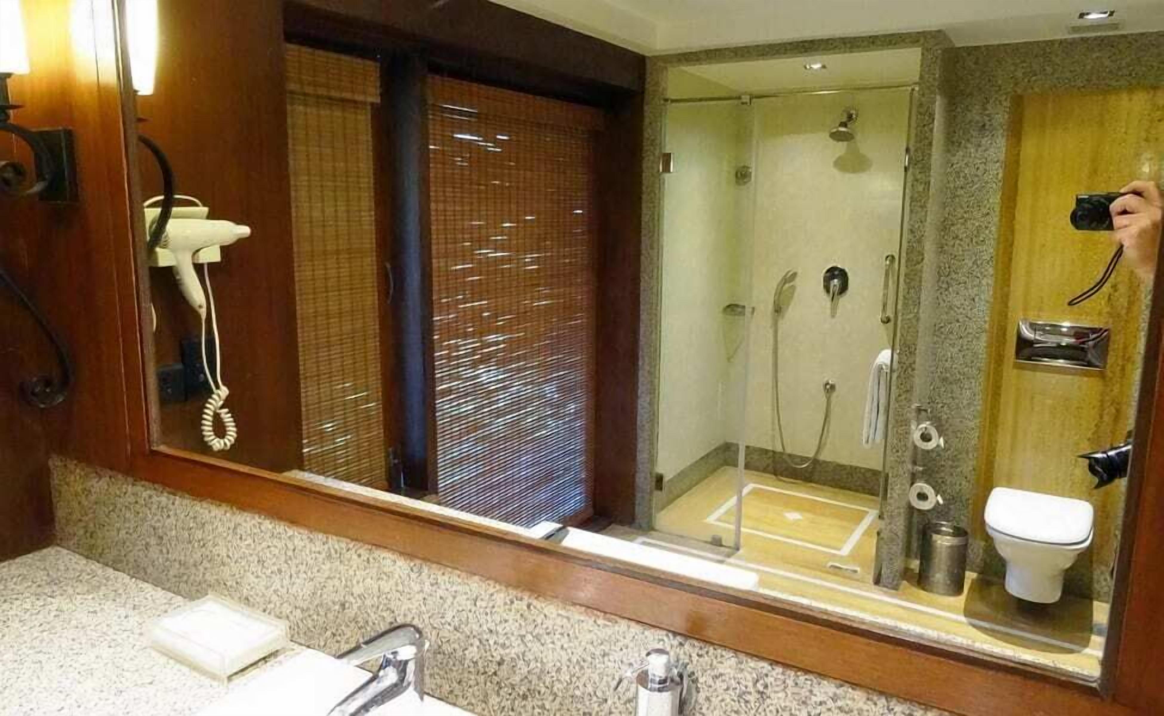 Baño con mampara de vidrio, secador de pelo y retrete visible en el espejo.