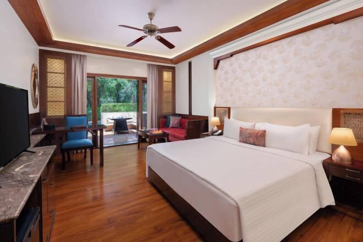 A hotel room with a large bed, a desk with a television, a chair, a sofa, and a balcony with a view.