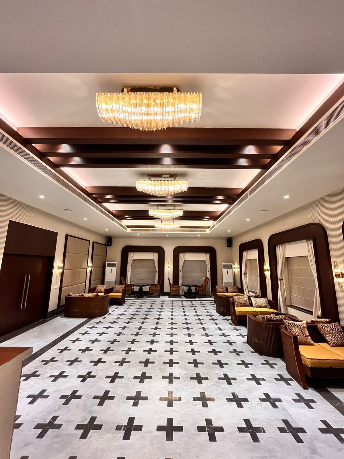 Un hall d’hôtel doté d’un tapis à motifs, de plusieurs espaces aménagés pour s’asseoir et d’un grand lustre.