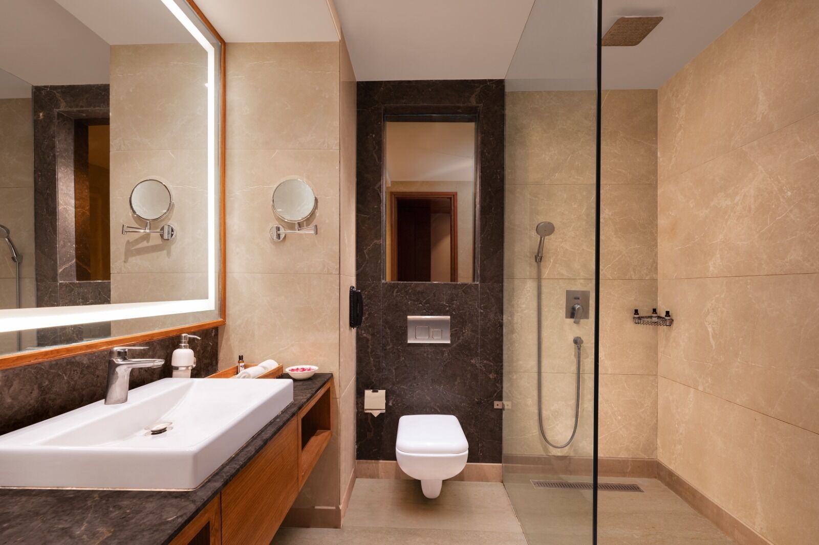 A modern bathroom with a large mirror, a white sink, a toilet, and a glass-enclosed shower.