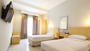 A hotel room with two beds, a television, a desk with a lamp, and a mirror. - Triniti Hotel Batam (Batam)