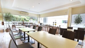 A spacious indoor dining area with multiple tables and chairs, large windows, and potted plants. - Triniti Hotel Batam (Batam)
